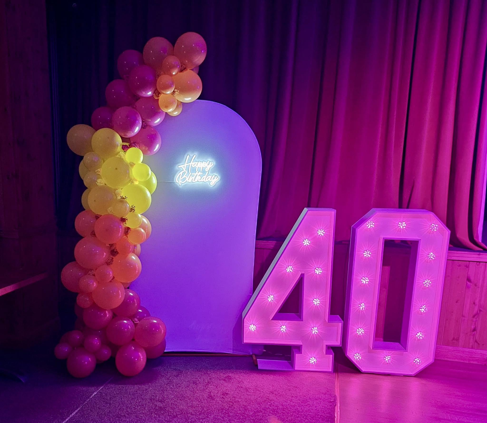 Pink light-up 40 numbers with a rainbow balloon garland and Happy Birthday neon sign