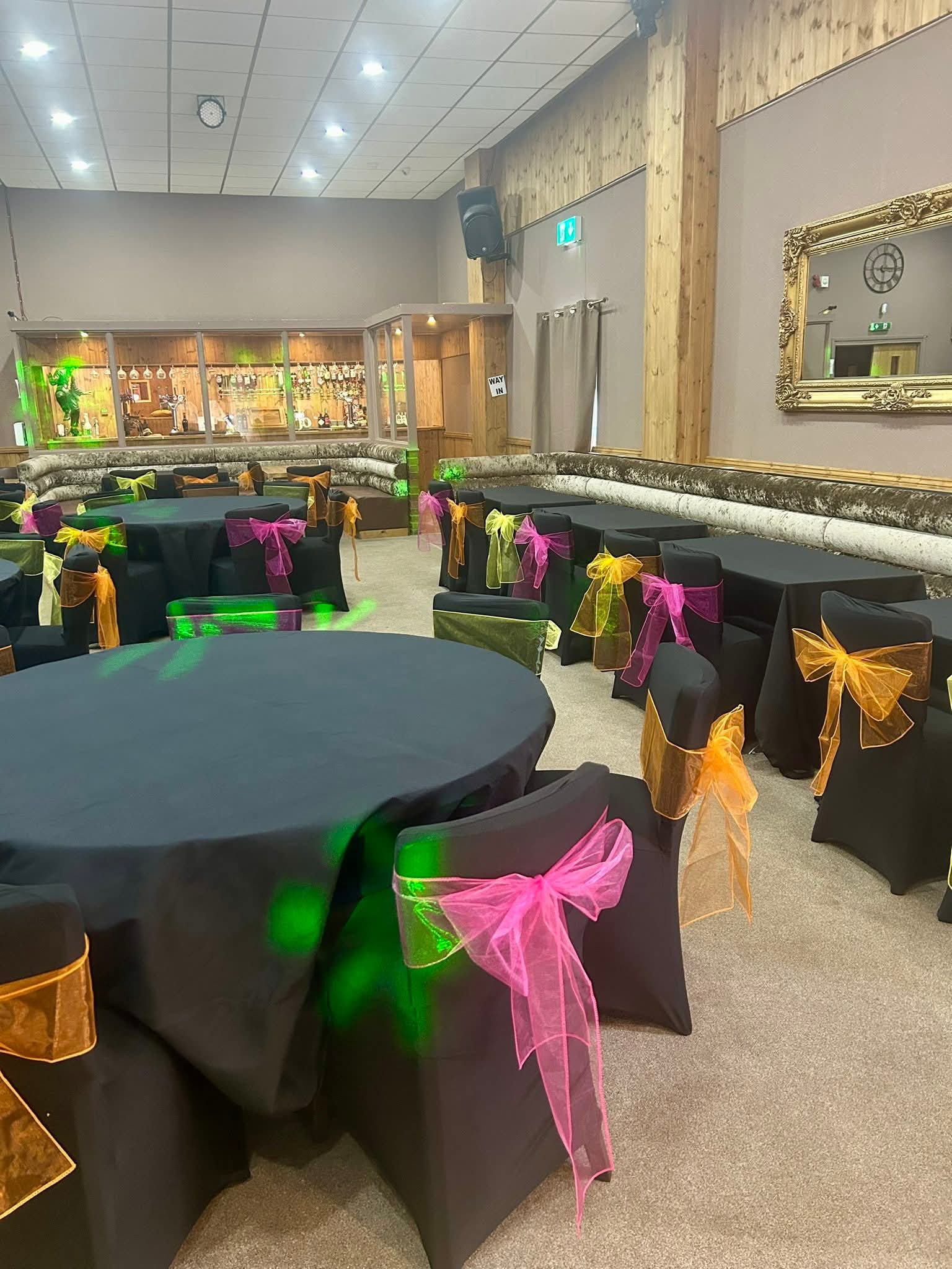 Function room with black chair covers and pink, orange, yellow and green sashes