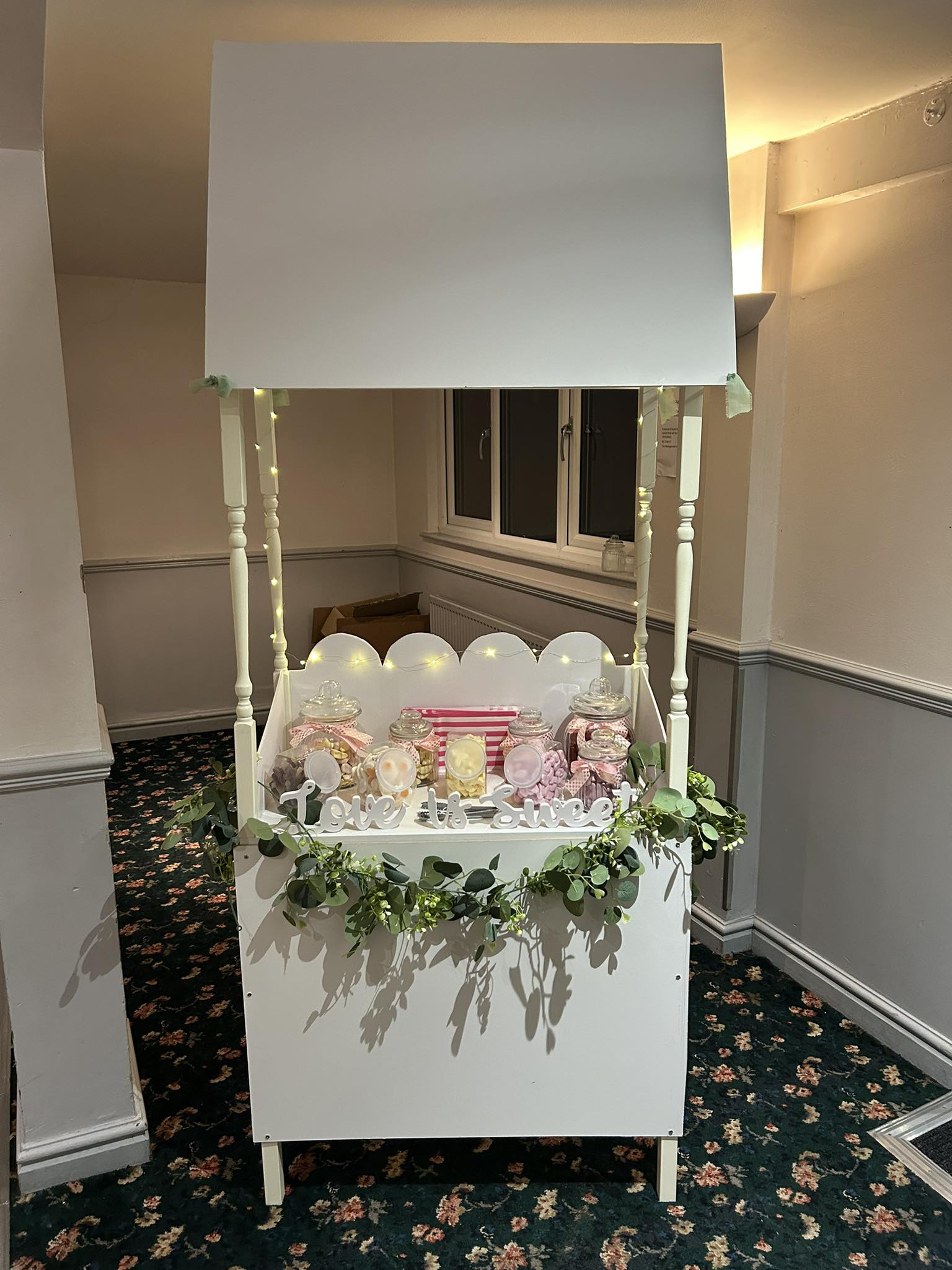 White sweet cart with fairy lights and jars of sweets, dressed with greenery