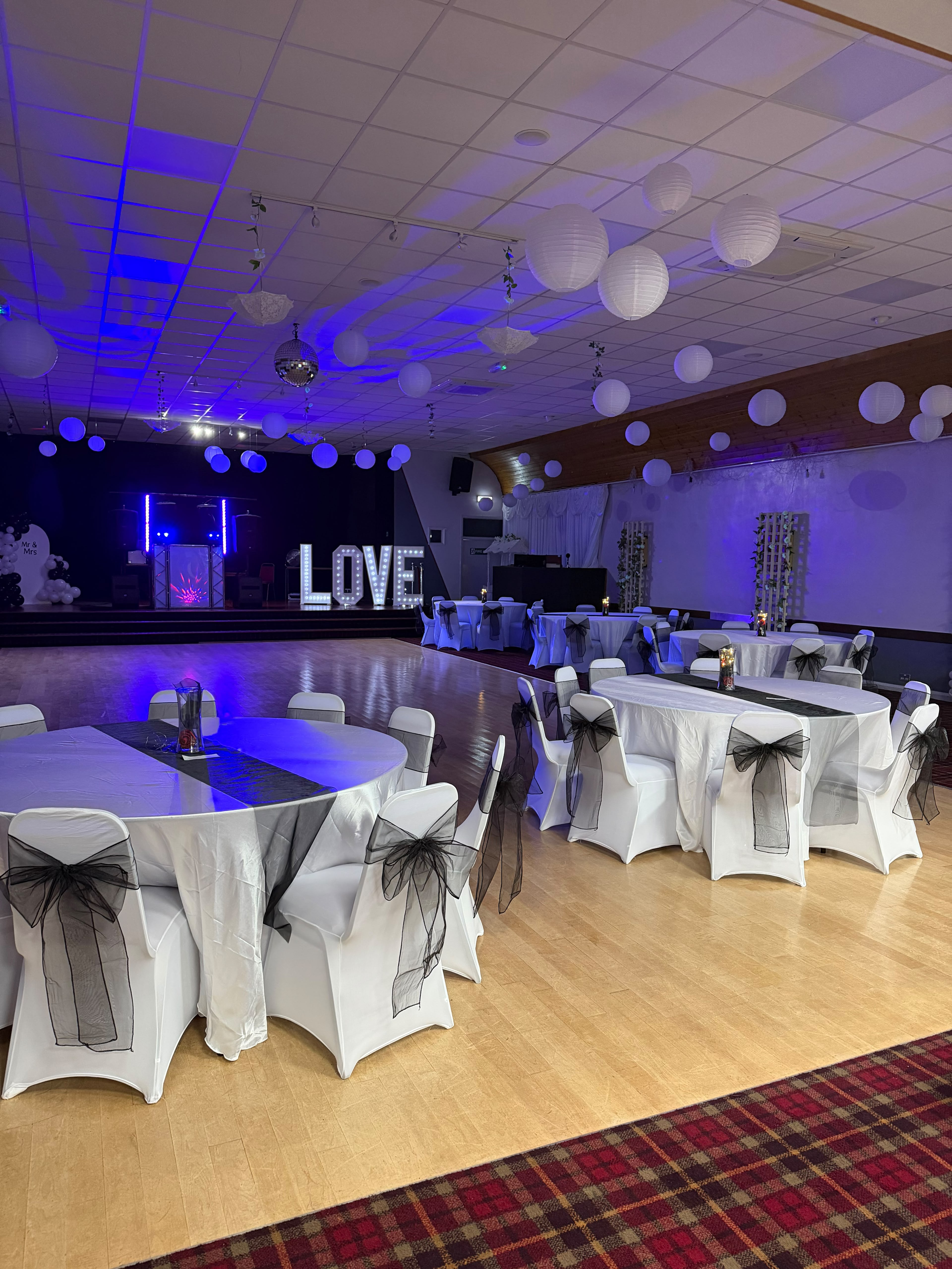 Wedding reception with white chair covers, black sashes, paper lanterns and light-up LOVE letters