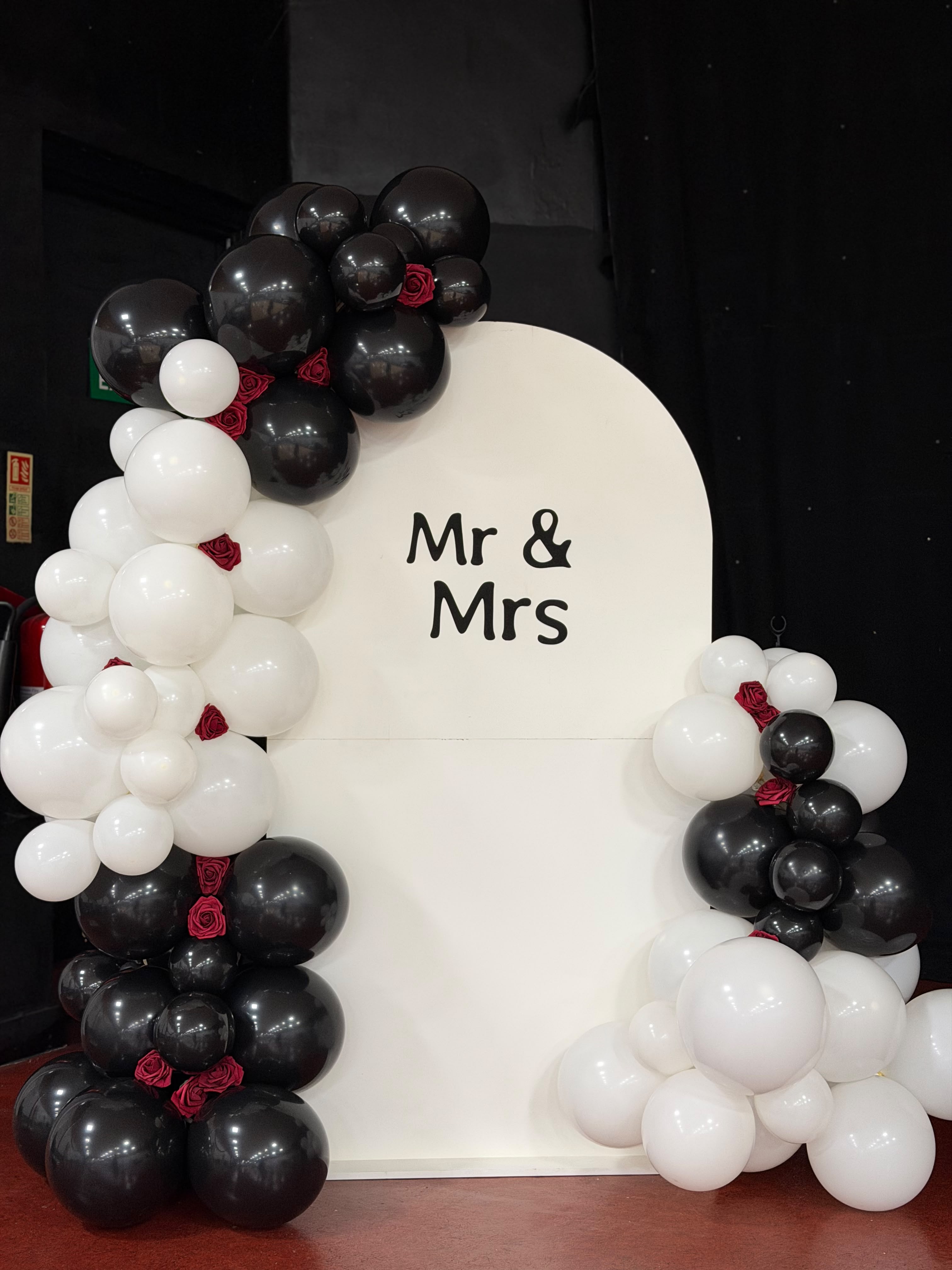 White Mr and Mrs backdrop with black and white balloon garland and burgundy roses