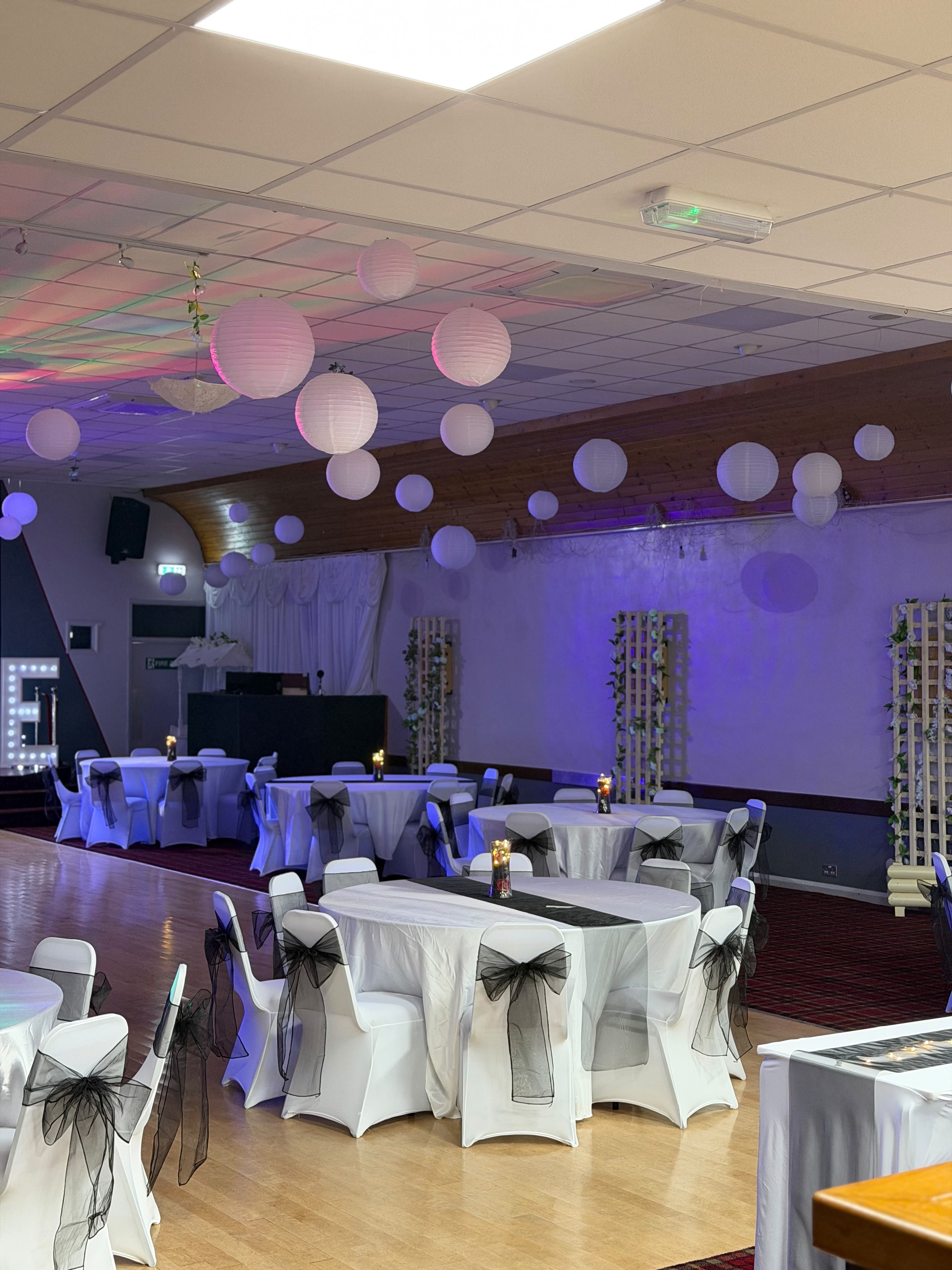 Wedding breakfast tables with white linens, black organza sashes and hanging paper lanterns