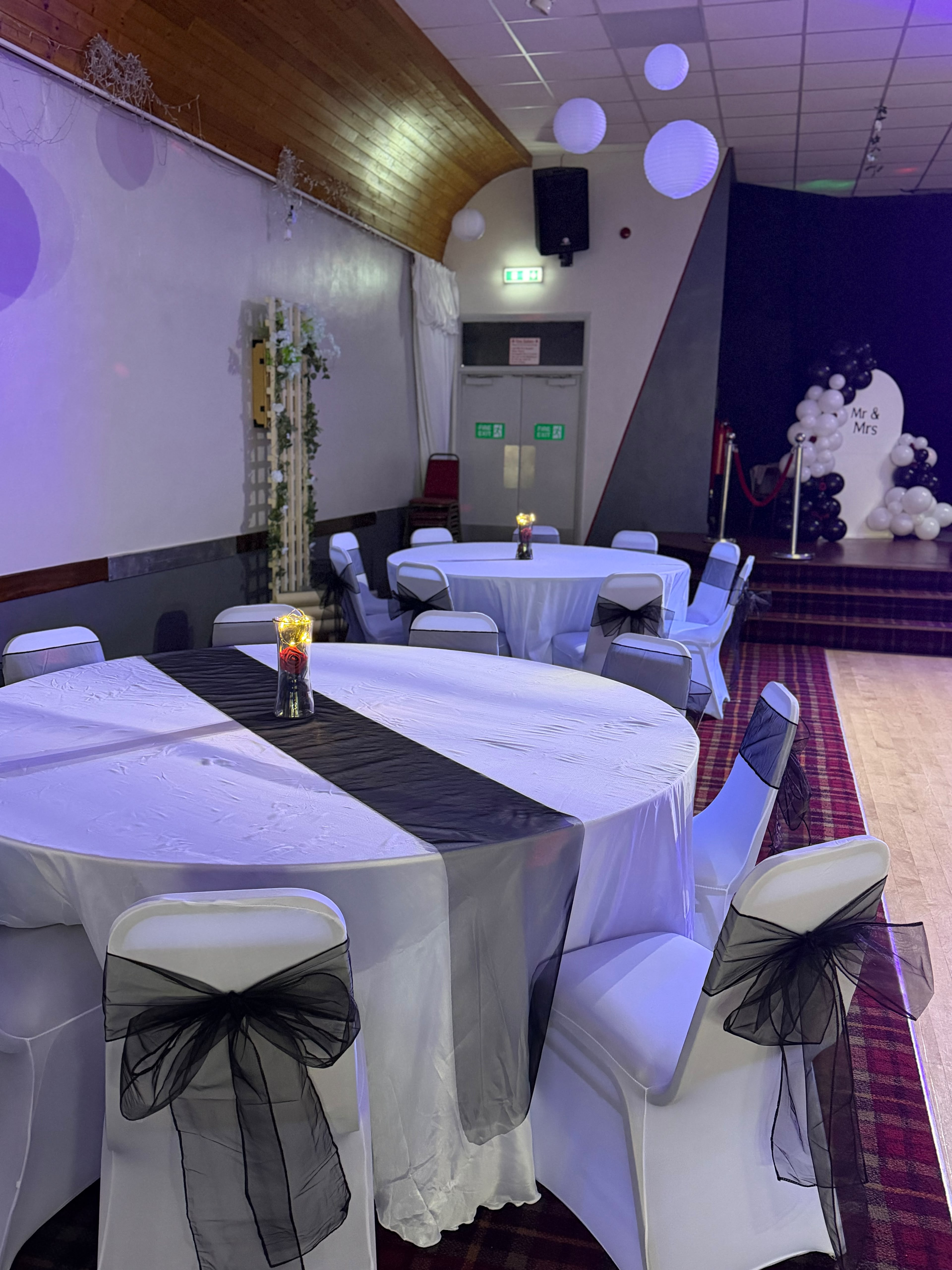 Round tables with black runners and organza bows, Mr and Mrs backdrop on the stage